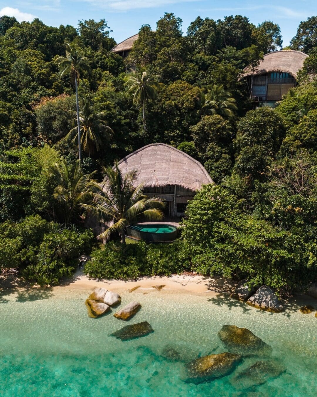 Cempedak Island villas set along a quiet beachfront, surrounded by dense tropical forest and clear turquoise water.