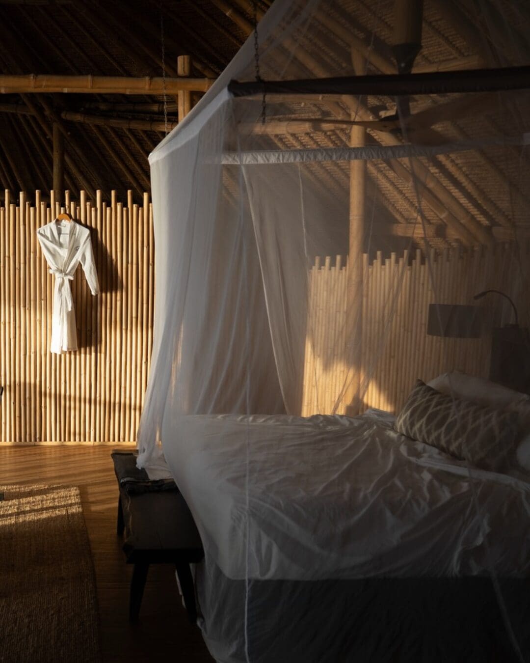 An open-air bedroom at Cempedak Island with bamboo walls, a canopy bed, and soft natural light filtering through the space.
