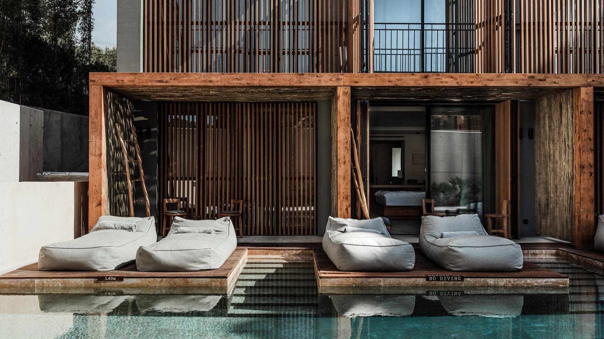 Poolside suites at OKU Ibiza with wooden terraces, cushioned loungers, and private swim-up access in a minimalist setting