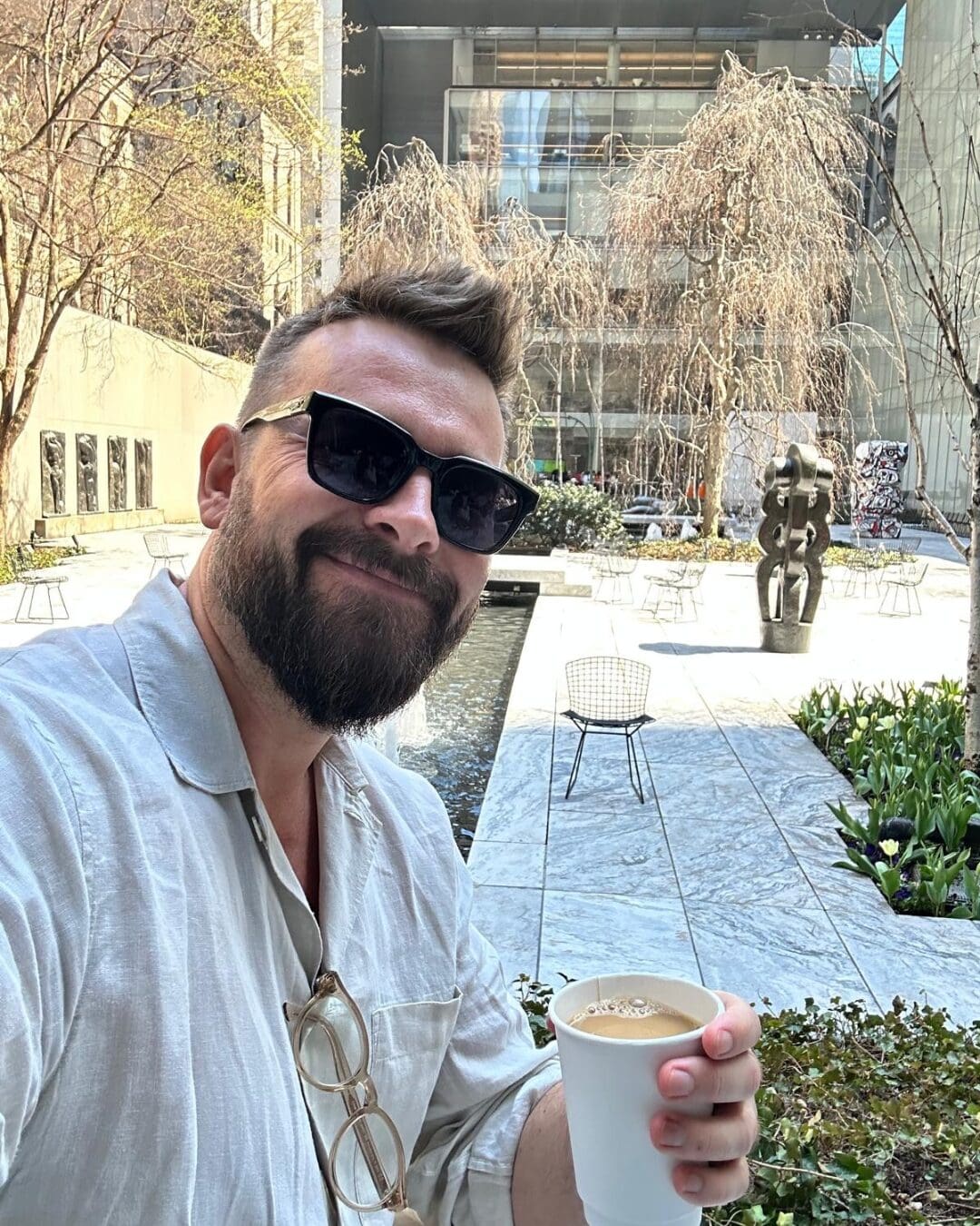 Guest enjoying coffee in a modern sculpture garden courtyard with water feature and spring trees in bloom