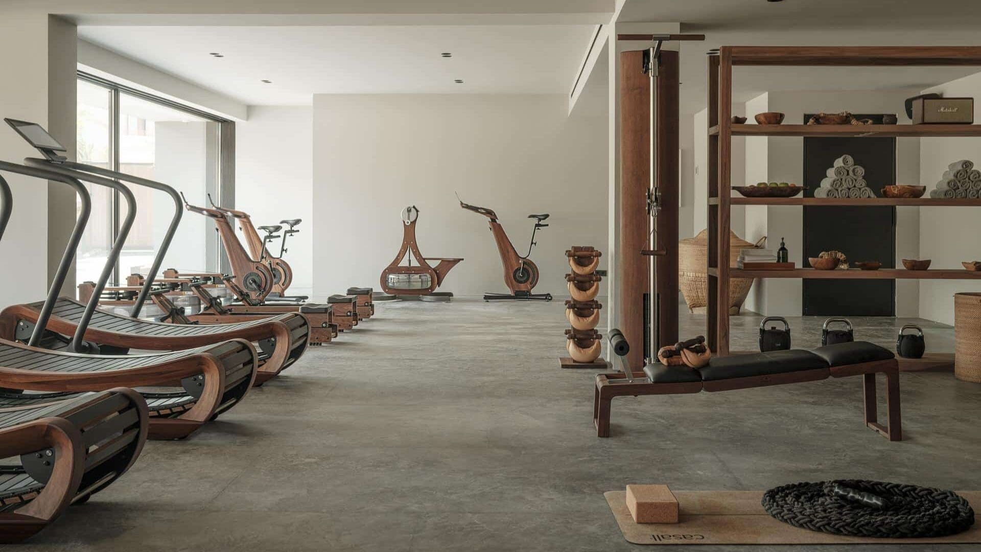 Minimalist gym at OKU Ibiza, Spain featuring wooden treadmills, bikes, and strength equipment in a light-filled space with natural materials and a calm, open layout.