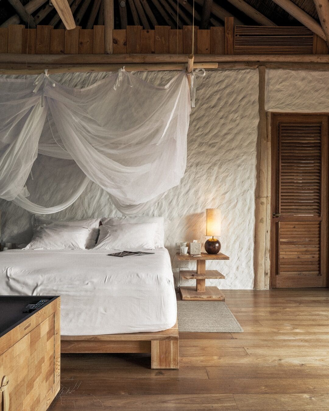 Natural wood and white bedroom with draped canopy bed and textured walls at Soneva Fushi villa