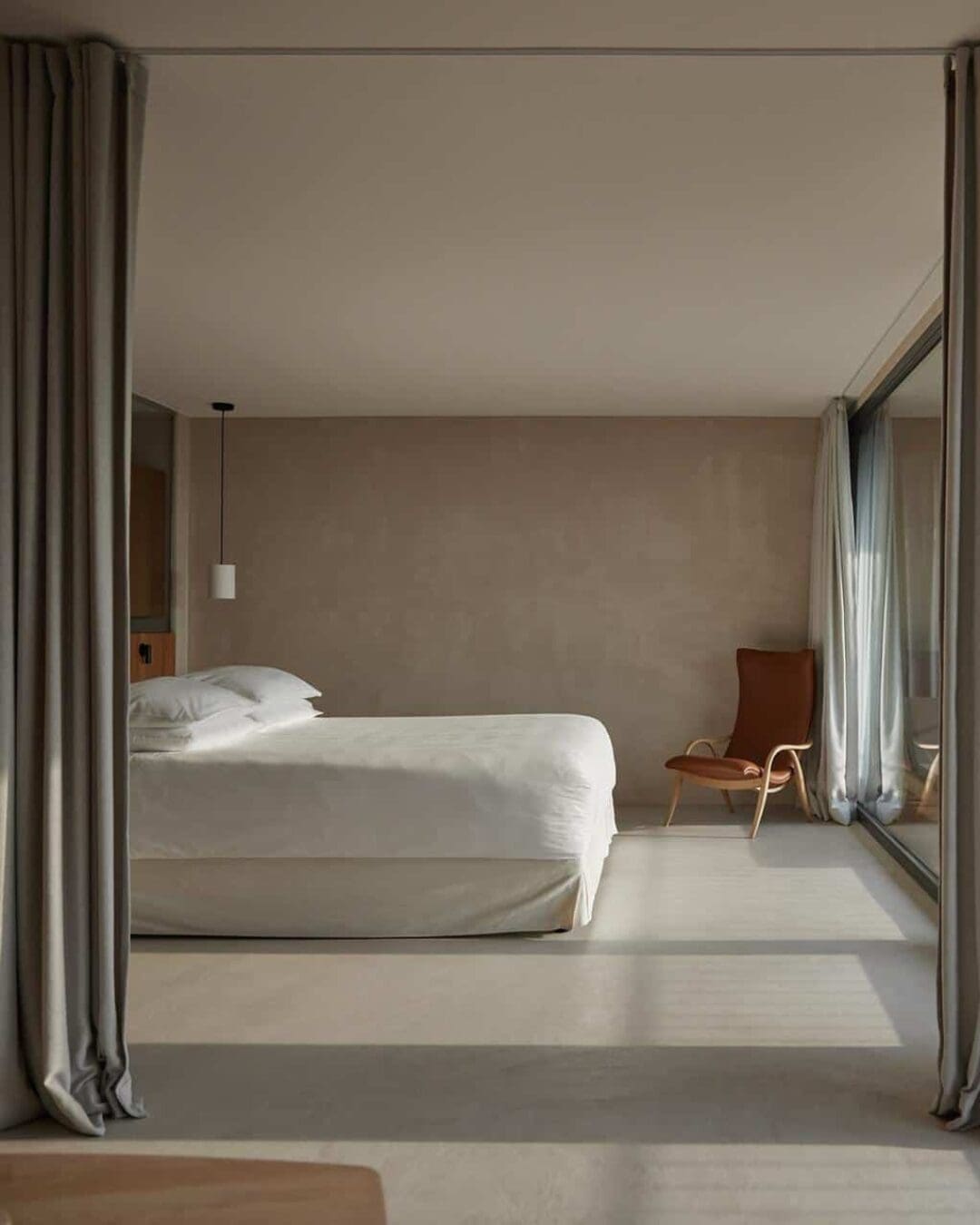 A minimalist bedroom at Saltus with soft neutral tones, floor-to-ceiling windows, and simple furnishings designed to maximise light and space.