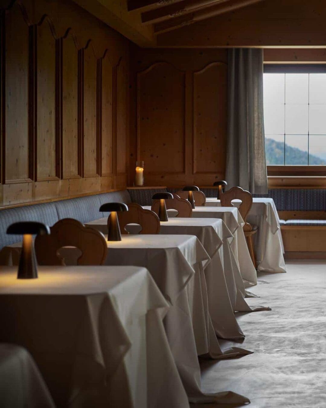 A warm, wood-lined restaurant at Saltus with simple table settings, soft lighting, and views out to the mountains.