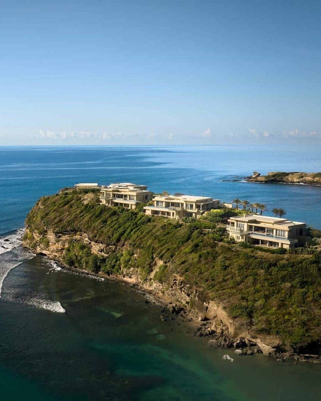 Six Senses La Sagesse set along a rugged coastline, with villas positioned above the sea and surrounded by natural greenery.