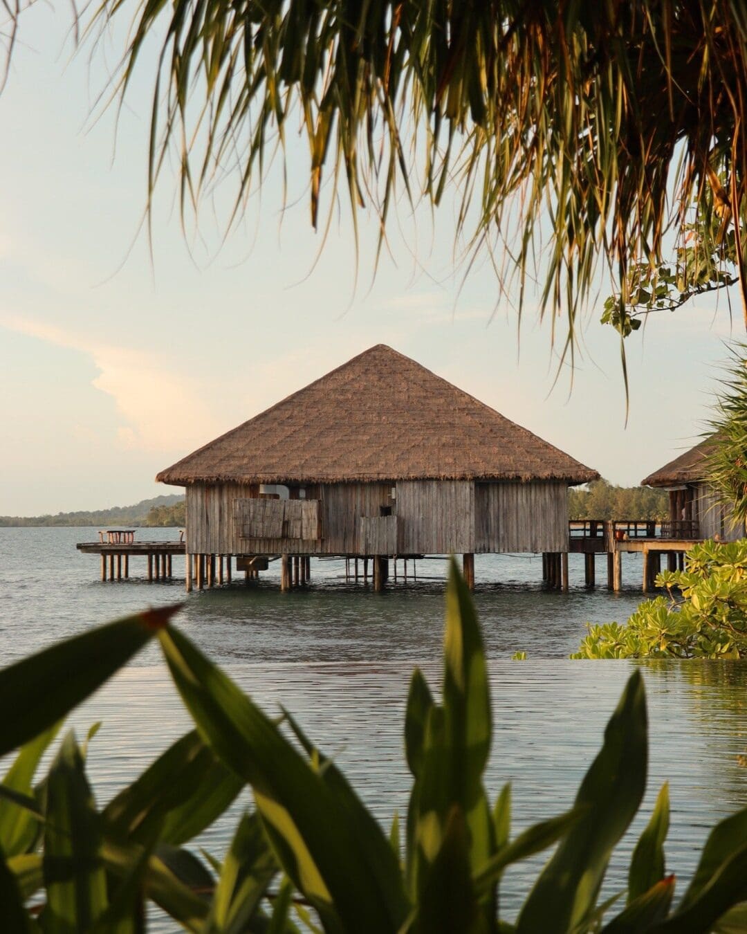 Thatched overwater villa framed by tropical foliage, set above calm ocean at Song Saa Private Island, Cambodia